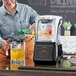 A woman pouring juice into an AvaMix commercial blender on a counter.