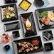 A table with Acopa glossy black square stoneware bowls filled with food.