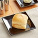 A piece of bread on an Acopa glossy black square stoneware plate with butter.