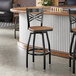 A black metal bar stool with a cross back design and a vintage wood seat.