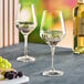 Two Acopa Silhouette wine glasses filled with wine next to a plate of grapes and a bottle.