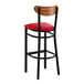 A bar stool with a black metal frame, red vinyl seat, and a curved vintage wood backrest.