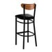 A black metal bar stool with a black vinyl seat and a curved vintage wood backrest.