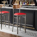 Two Lancaster Table & Seating red vinyl bar stools with vintage wood backs at a bar counter.