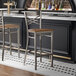 A metal bar stool with a cross back design and a vintage wood seat.