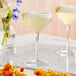 A pair of Acopa Silhouette coupe glasses filled with yellow liquid on a table with food.