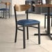 A Lancaster Table & Seating Boomerang Series chair with a navy vinyl seat and vintage wood back at a table in a restaurant.