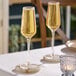 Two Acopa Silhouette champagne flutes on a table with candles.