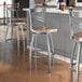 A Lancaster Table & Seating swivel bar stool with a wooden seat and metal back.