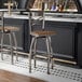 A metal bar stool with a cross back design and a vintage wood seat, featuring a swivel function.