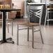 A metal cross back chair with a clear coat finish and a vintage wood seat.