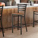 A black metal ladder back bar stool with a vintage wood seat placed at a counter.