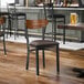 A black metal chair with a dark brown vinyl seat and a curved vintage wood backrest.