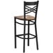 A black metal bar stool with a cross back design and a vintage wood seat.