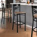 A black metal bar stool with a cross back design and a vintage wood seat.