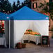 A blue and white 10' x 10' pop-up canopy tent with straight legs and four side walls, set up as a market stall.