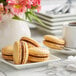 A white plate with three White Toque French caramel macarons and a cup of coffee on a table.