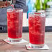 A bartender pours a red drink into an Arcoroc ArcoPrime beverage glass on a table with another glass of red liquid.