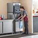 A woman in a red apron standing in front of a Scotsman air cooled ice machine in a professional kitchen.