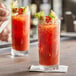An Arcoroc ArcoPrime beverage glass filled with a red cocktail, ice, and oranges on a table.