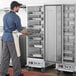 A man in a blue shirt and apron using a Main Street Equipment heated holding cabinet to hold a tray of food.