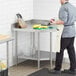 A man in a chef's outfit standing at a Regency stainless steel corner work table.