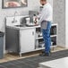 A man standing in a professional kitchen next to a Regency stainless steel beverage table with a sink.