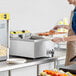 A man in an apron using a Carnival King Funnel Cake Fryer in a school kitchen.