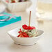 A small white Tablecraft mini melamine bowl with food in it on a table.