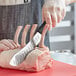 A person using a Mercer Culinary butcher knife to cut meat.