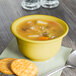 A Fiesta sunflower china bouillon filled with soup and a cracker on a napkin.