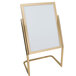 An Aarco brass double pedestal poster stand with a white board on it.