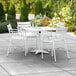 A white table with umbrella hole and 4 chairs on a patio.