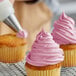 A person decorating a cupcake with Rich's Bettercreme pink whipped icing.