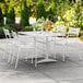 A white Lancaster Table & Seating outdoor dining table with chairs on a patio.