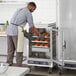 A man putting food in a ServIt holding cabinet with a clear door.