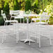 A Lancaster Table & Seating white bar height outdoor table with 4 white bar stools on a patio.