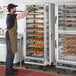 A man wearing a brown apron putting trays of pastries in a ServIt holding and proofing cabinet.