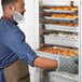 A man in a blue apron opening the clear door of a ServIt holding and proofing cabinet.