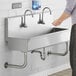 A man washing his hands in a Regency stainless steel multi-station hand sink.