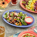 An oval purple melamine platter with a salad and tortilla on it.