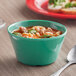 A green Acopa Foundations melamine bouillon cup filled with soup on a table with a spoon.