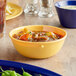 An Acopa Foundations yellow melamine nappie bowl filled with soup on a table.