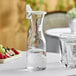 A Tablecraft polycarbonate carafe with a resealable lid on a table next to glasses of water.