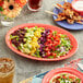 An Acopa orange melamine oval platter with a bowl of salad with vegetables on a table.