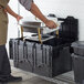 A person holding a black Lavex industrial storage tote filled with food.