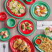 A table with green Acopa melamine plates of food, including a plate of food with lettuce and sauce.