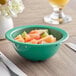 A green Acopa Foundations melamine bowl filled with fruit on a table.