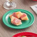 A piece of food wrapped in ham on a green Acopa Foundations melamine plate.