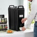 A man pouring coffee into a Cambro black insulated beverage dispenser.